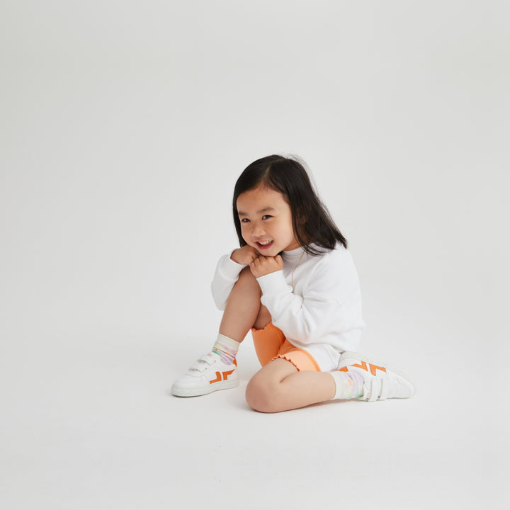 Children's trainers being worn. White and orange velcro trainers